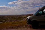 Experience epic views with an **RV rental**! A camper van overlooks a vast badlands landscape under a cloud-filled sky.