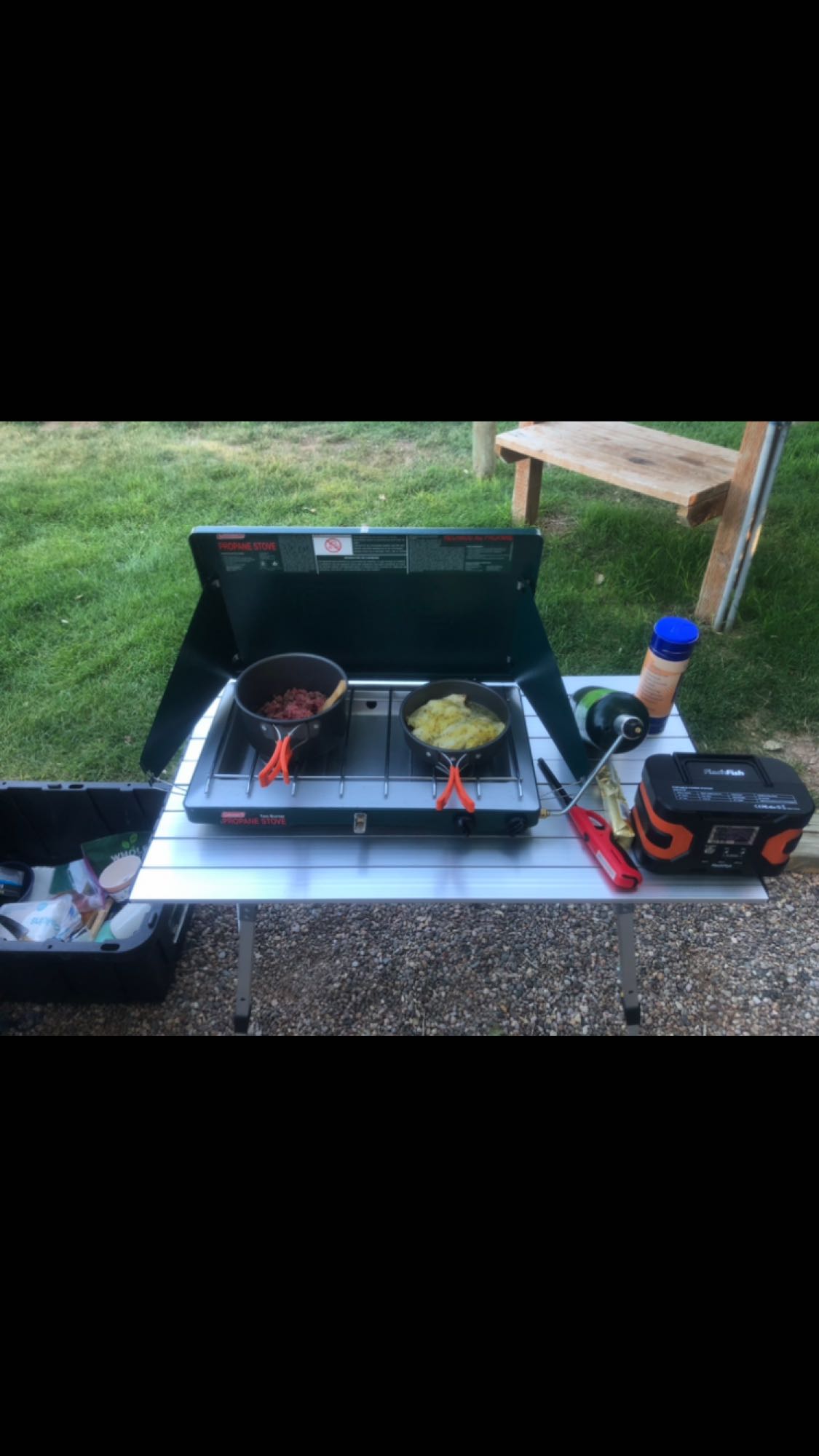 Cooking dinner on a portable propane stove with two pots, camping essentials, and power station on a table during an rv rental trip.