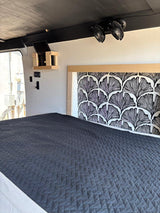 This RV rental's compact bedroom features a dark gray quilted bed, stylish patterned headboard, and overhead fans.