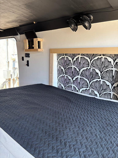 This RV rental's compact bedroom features a dark gray quilted bed, stylish patterned headboard, and overhead fans.