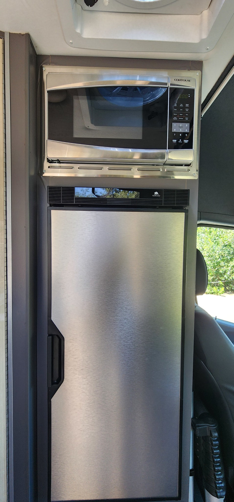 Compact RV rental kitchen featuring a stacked stainless steel Contoure microwave oven and Norcold refrigerator. — photo 10
