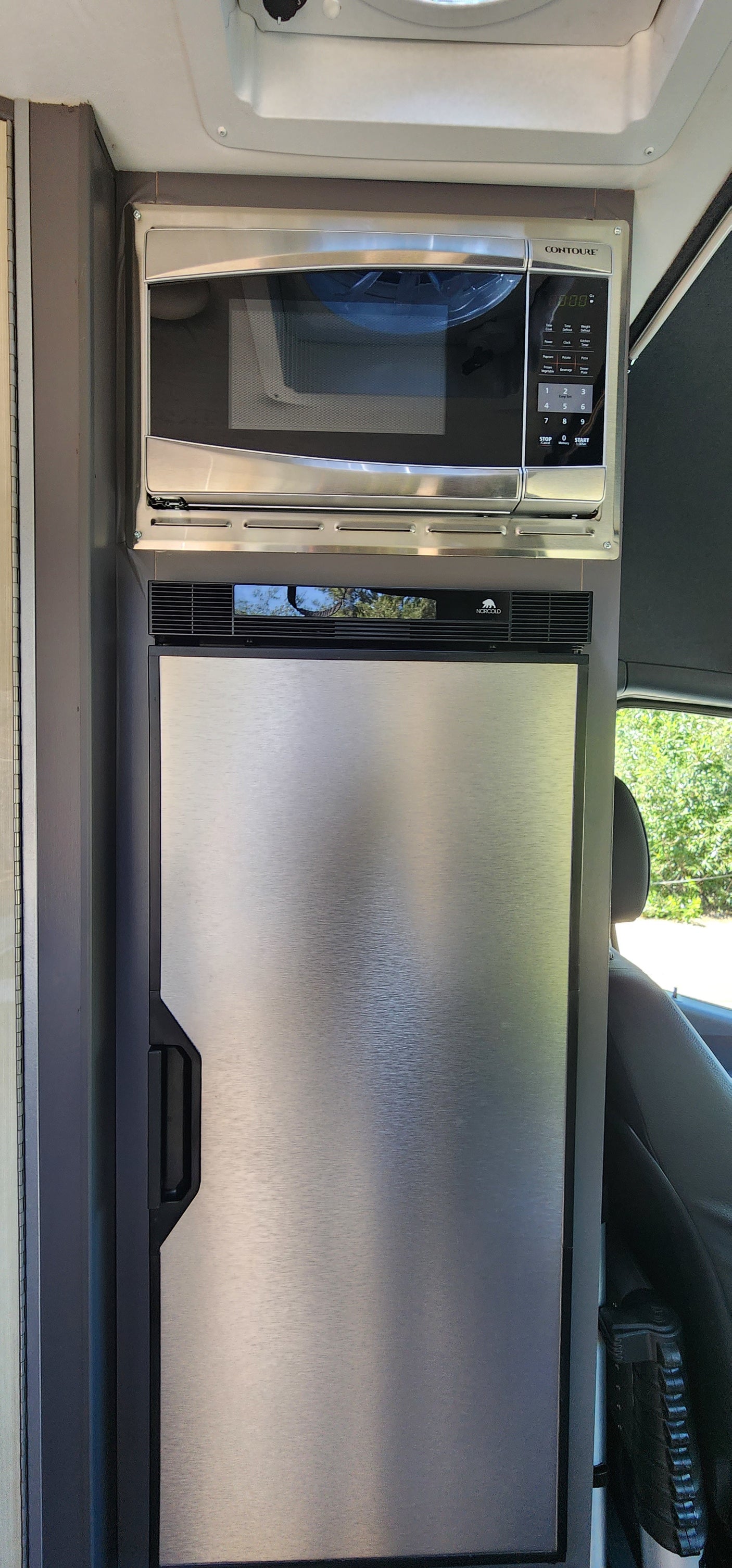 Compact RV rental kitchen featuring a stacked stainless steel Contoure microwave oven and Norcold refrigerator.