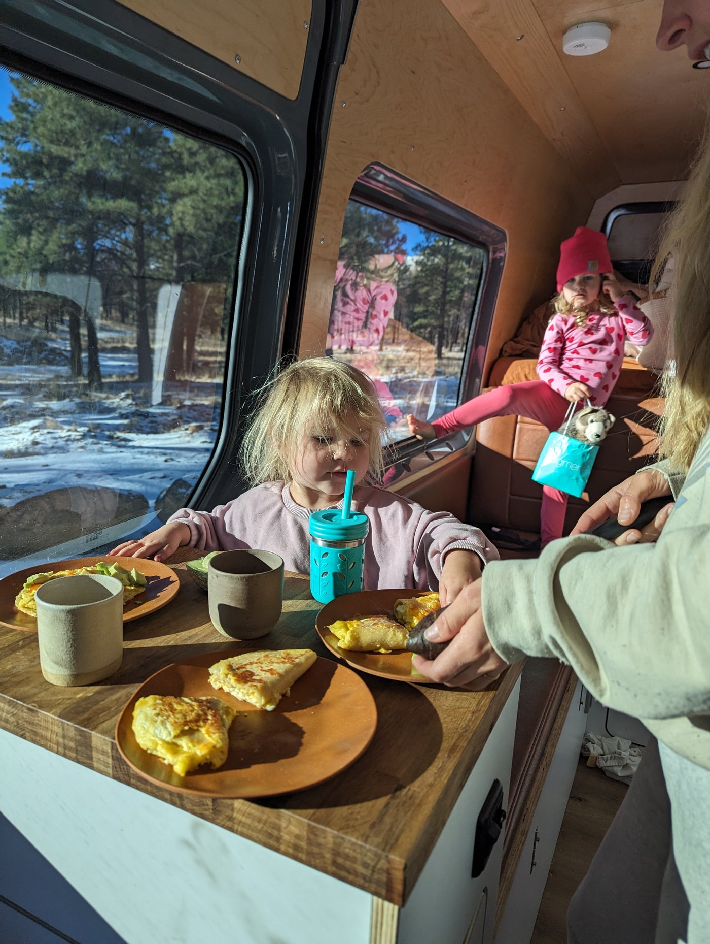 Family enjoys breakfast inside a cozy RV rental. Kids eat eggs & avocado with a snowy forest view. — photo 5