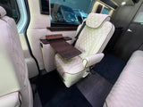 Inside a luxury RV rental: cream diamond-quilted captain's chair, dark wood table with cupholder, and comfortable rear seating.