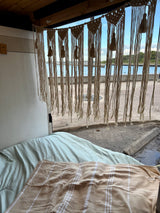 Cozy RV rental interior with a bed, macrame decor, and a scenic water view from the open back.