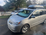 A silver Toyota minivan with a frosted windshield and roof cargo box, parked outside. Explore various travel vehicles, from this minivan to an RV rental.