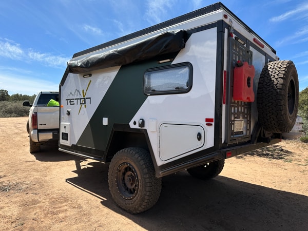 Explore with this Teton RV rental! A white & green off-road camper trailer, with rugged tires, is towed by a truck on a dirt path. — photo 13
