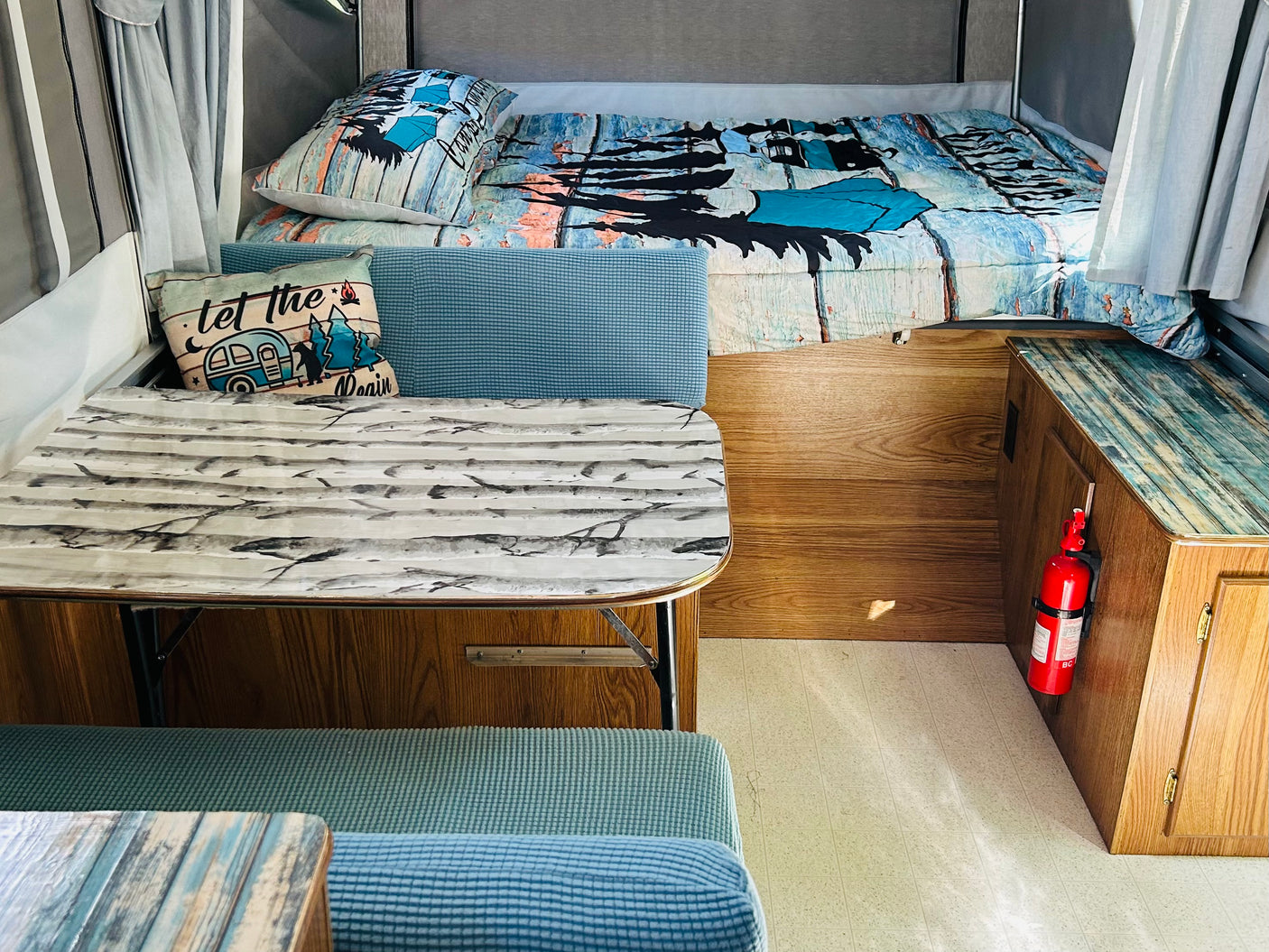 "Let the adventure begin" in this cozy RV rental, featuring a bed, dinette with patterned table, and blue seating.