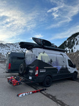 Two adventure RV rental vans. The custom-painted van has a kayak, ski, & activity graphics; parked in snowy mountains.