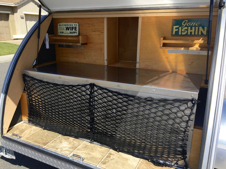 This rv rental teardrop camper features an open galley kitchen with custom signs, storage, and a practical cargo net.