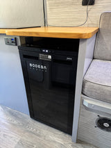 This RV rental features a built-in Bodega Cooler, control panel, and comfy seating inside a modern camper van.