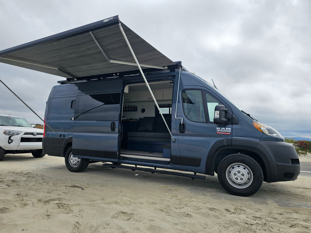 Explore the coast! This blue Ram ProMaster camper van RV rental with an extended awning is ready for beach adventures.