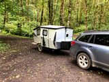 Car towing an RV rental camper in a lush, mossy forest campsite, perfect for nature getaways.