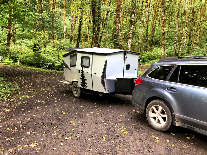 Car towing an RV rental camper in a lush, mossy forest campsite, perfect for nature getaways.