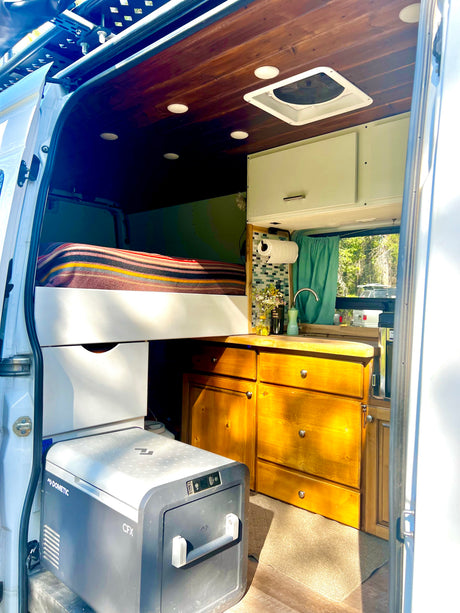 Inside a spacious RV rental camper van: elevated bed, full kitchen, and Dometic fridge. Perfect for mobile adventures.
