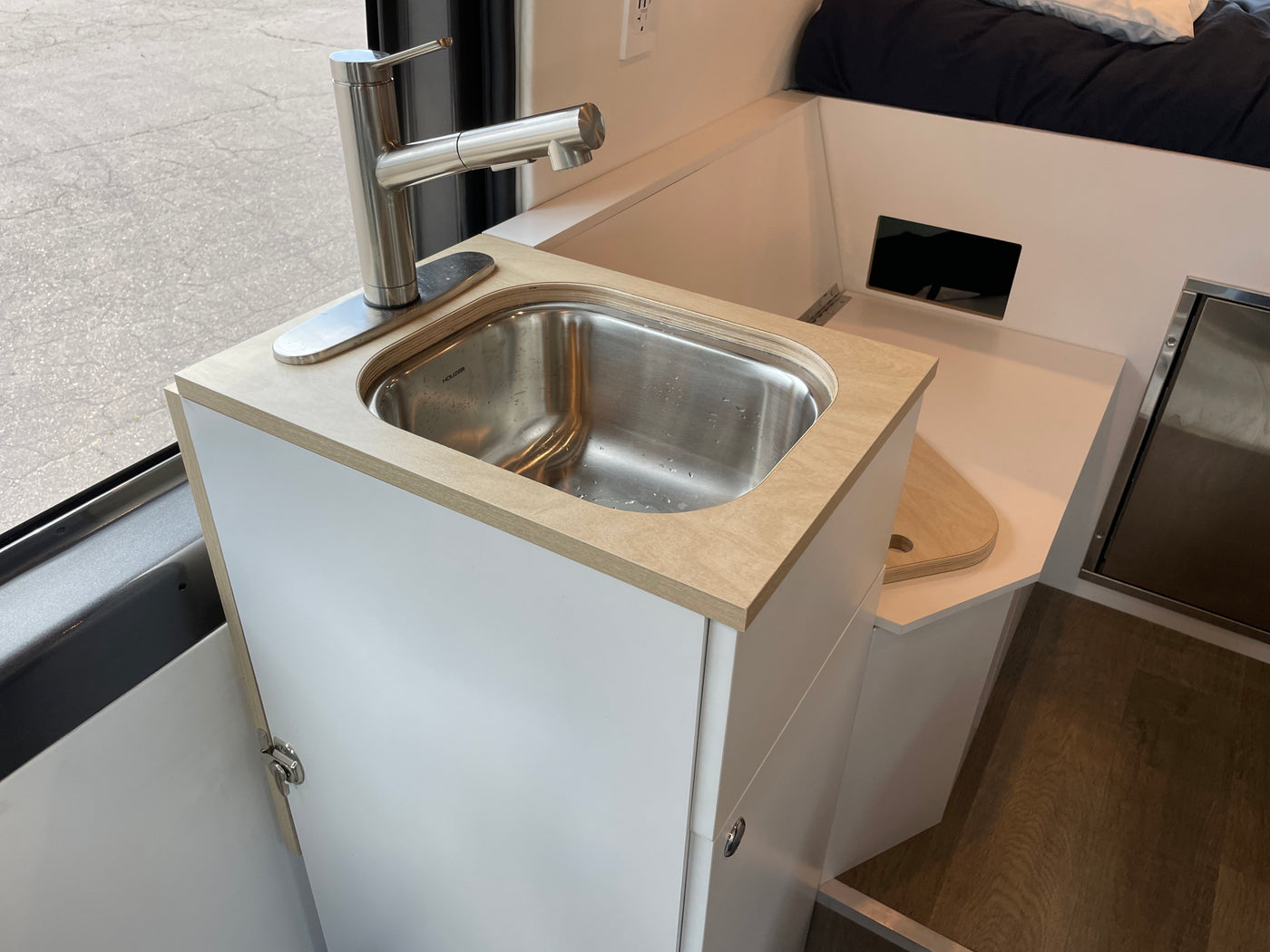 Cozy RV rental kitchen featuring a stainless sink, modern faucet, and light wood counters in a custom camper van. — photo 16