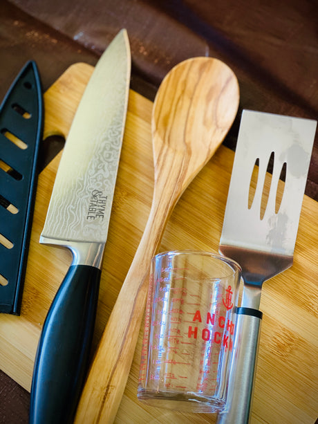 Kitchen tools for your RV rental: THYME & TABLE knife, wooden spoon, spatula, and Anchor Hocking measuring cup on a board.