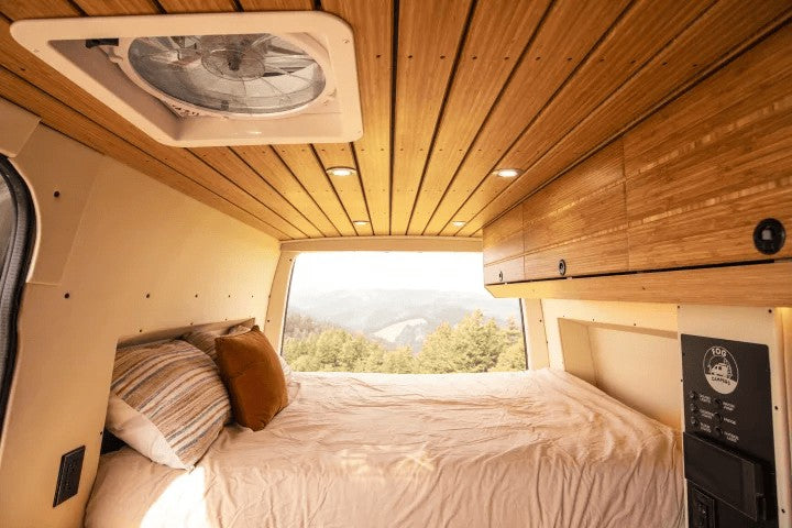 Cozy rv rental camper van interior: a bed with mountain views, bamboo ceiling, fan, and controls for a comfortable escape.