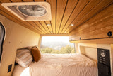 Cozy rv rental camper van interior: a bed with mountain views, bamboo ceiling, fan, and controls for a comfortable escape.