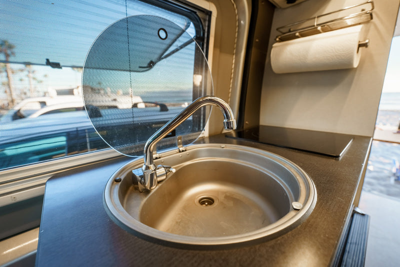 Inside an RV rental: compact kitchen with sink, faucet, stovetop, paper towels, and screened window. — photo 19
