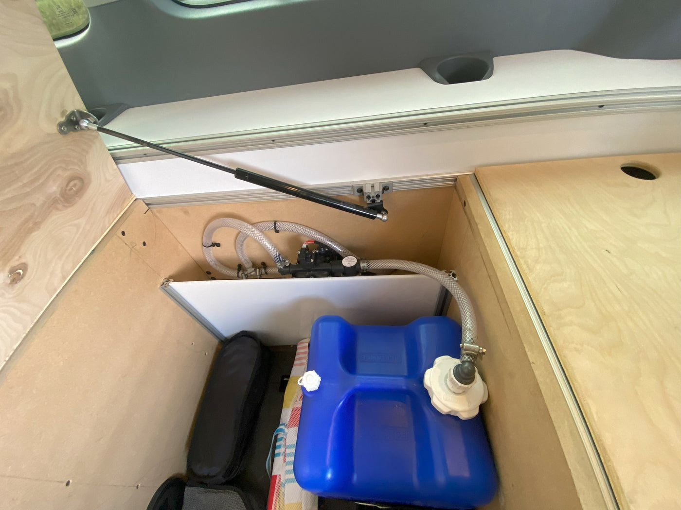 RV rental: Inside, a clean water system for travelers. Blue tank, pump, and hoses are visible within the wood and aluminum storage. — photo 12