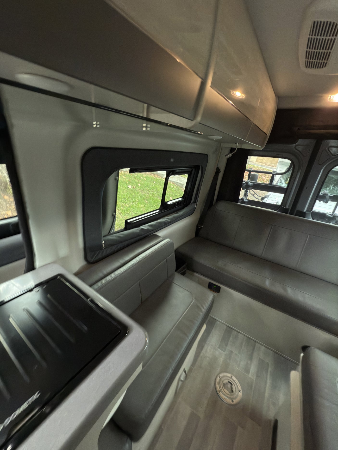 Spacious RV rental interior featuring modern gray seating, a compact kitchen area, and large windows. Perfect for trips!