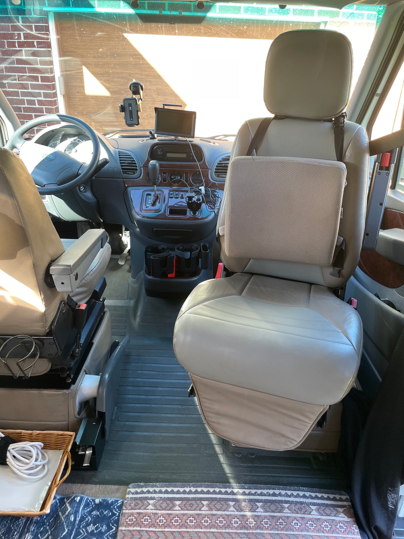 Spacious RV rental interior showing tan front seats, dashboard, steering wheel, and console. Bright sunlight fills the cockpit.