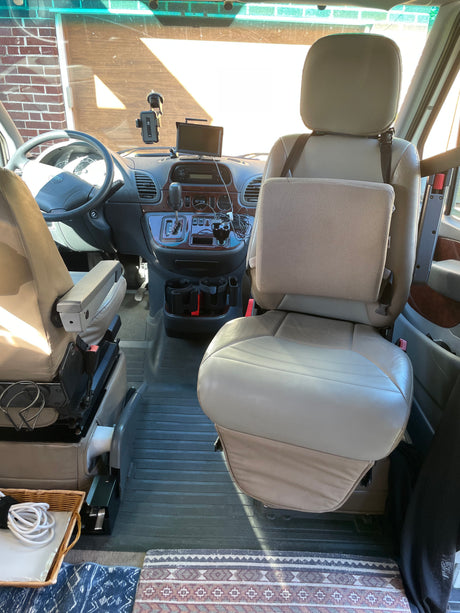 Spacious RV rental interior showing tan front seats, dashboard, steering wheel, and console. Bright sunlight fills the cockpit.