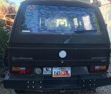 This dark VW Vanagon, a classic RV rental, shows its Utah plates & adventure stickers. Note the marine-themed rear window.