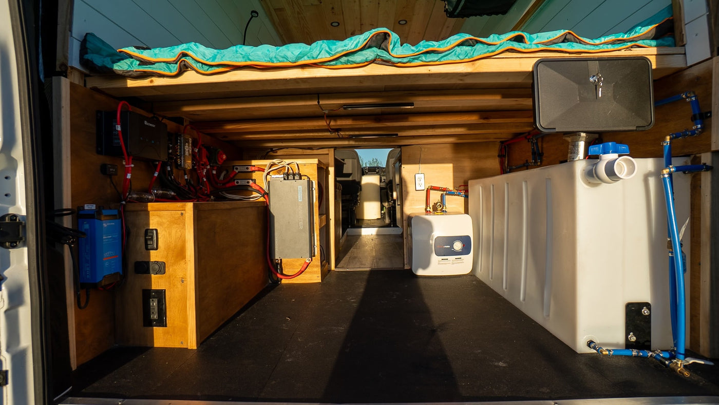 Rear view of an RV rental van conversion showing the organized electrical system, inverter, water tank, and heater for comfort. — photo 17