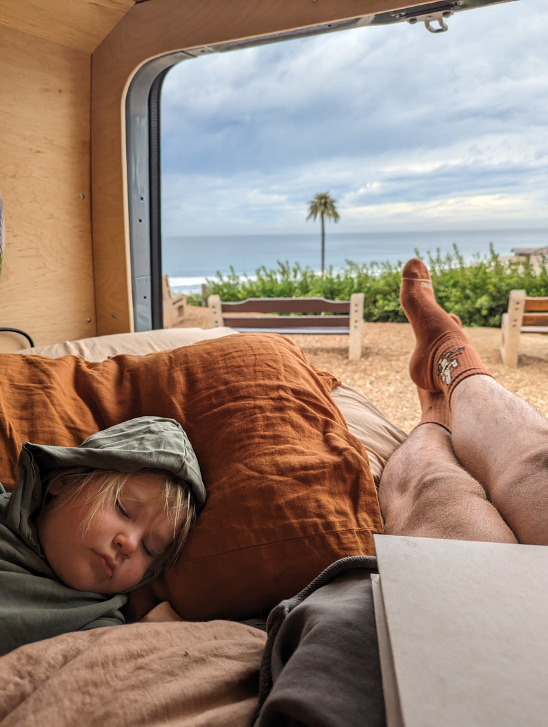 Relaxing in an RV rental: a child sleeps soundly while an adult's feet rest, overlooking a coastal ocean view. — photo 4