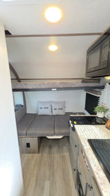 Compact rv rental interior features a bunk bed, convertible dinette, and kitchen with microwave/stove for small group travel.