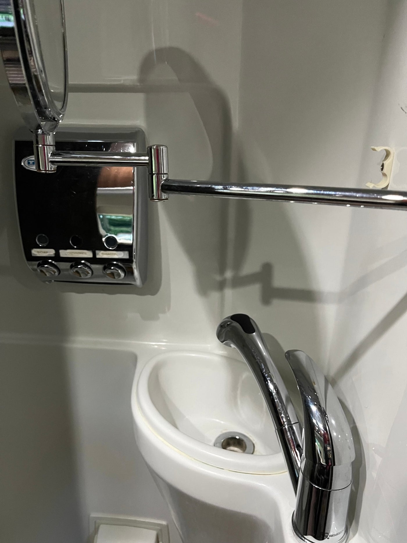 Compact RV rental bathroom with chrome faucet, mirror, multi-dispenser, towel bar, and hook over a small white sink. — photo 14
