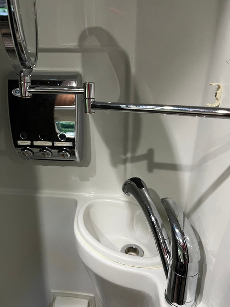 Compact RV rental bathroom with chrome faucet, mirror, multi-dispenser, towel bar, and hook over a small white sink.