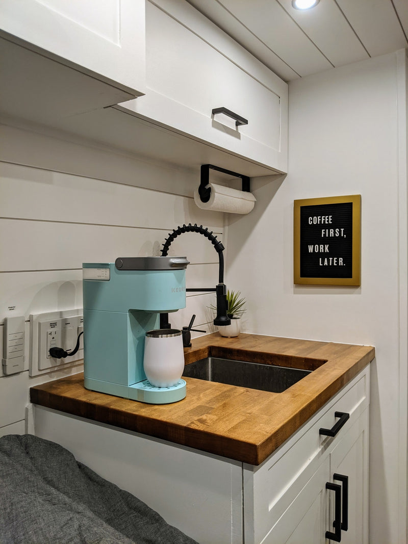 Modern compact kitchen in an **RV rental**, featuring a blue coffee maker, wood counter, sink, & "Coffee First" sign. — photo 19