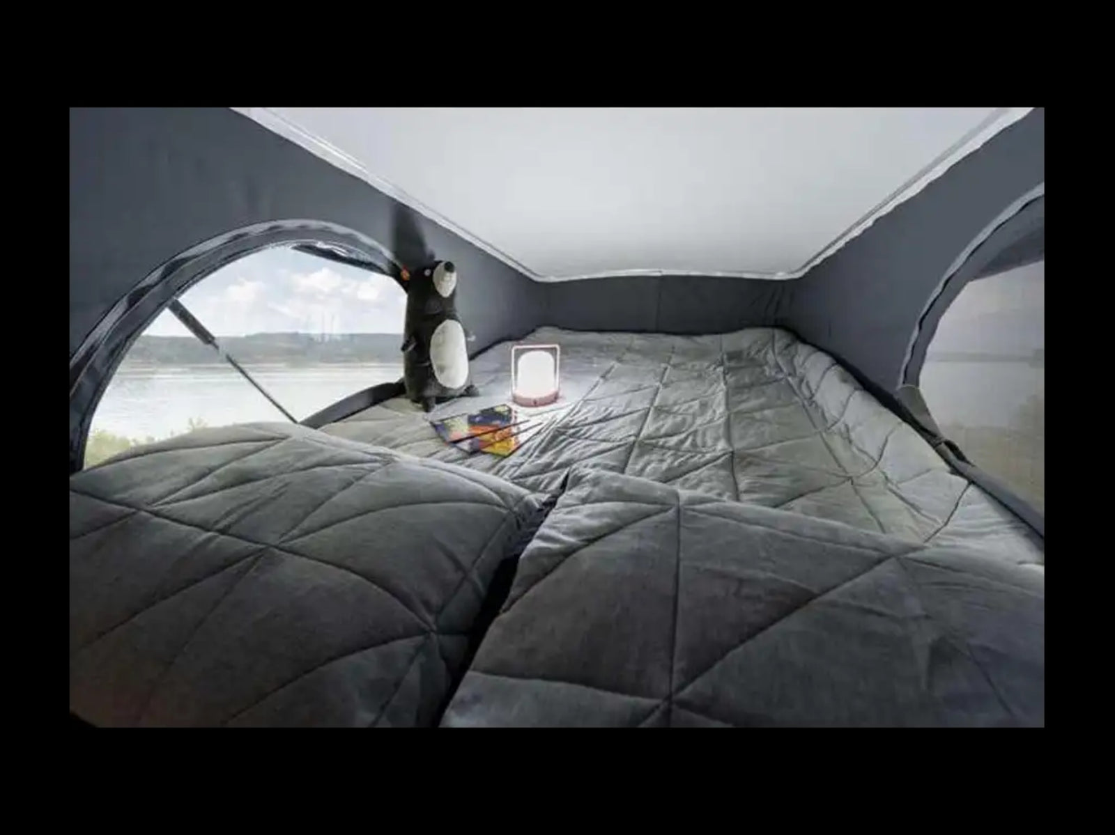 Cozy RV rental interior: quilted bed, large window with water view, plush toy, and lantern for comfy travel.