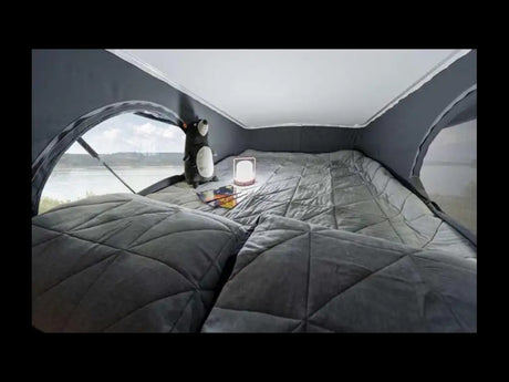 Cozy RV rental interior: quilted bed, large window with water view, plush toy, and lantern for comfy travel.