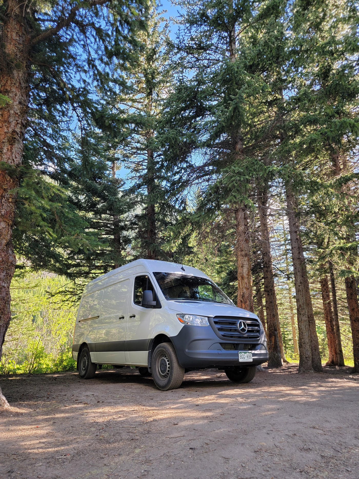 White Mercedes Sprinter camper van, perfect for your next RV rental adventure, parked on a dirt road among tall trees. — photo 3