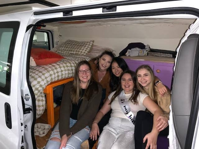 Friends enjoying an RV rental adventure inside a comfy converted van with bed and storage, perfect for group travel.