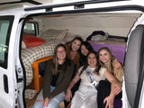 Friends enjoying an RV rental adventure inside a comfy converted van with bed and storage, perfect for group travel.