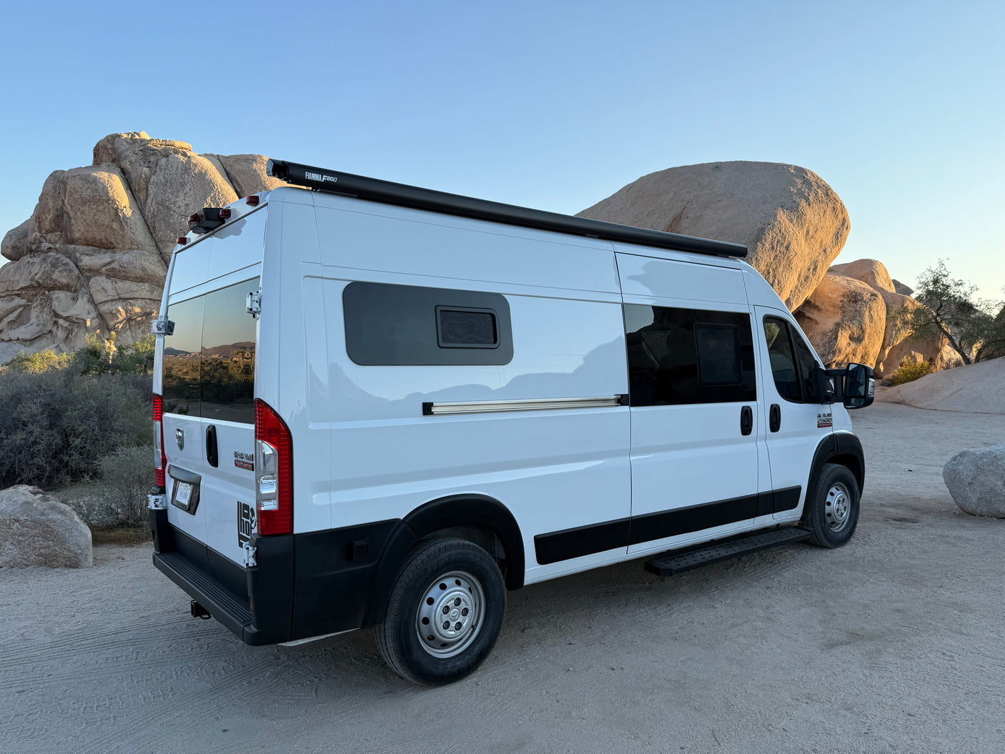 White RV rental camper van parked in a rugged desert landscape with immense rock formations. Plan your next adventure!