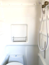 Inside an RV rental wet bath, showing a white shower, toilet, and storage rack. A compact, functional space for travel.