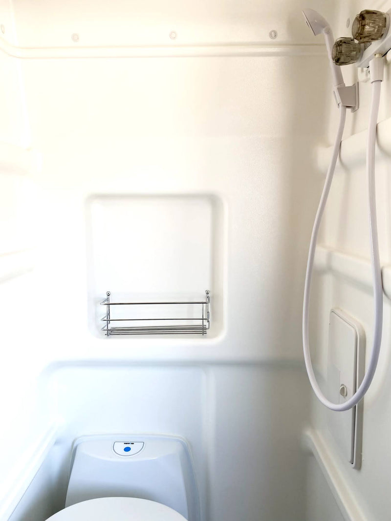 Inside an RV rental wet bath, showing a white shower, toilet, and storage rack. A compact, functional space for travel. — photo 12