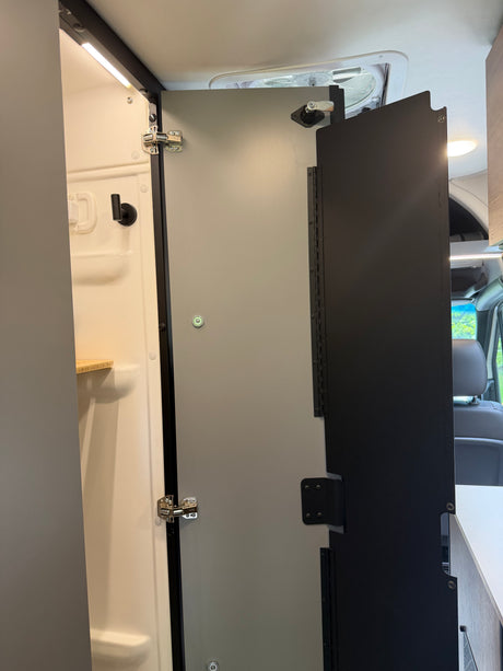 Compact RV rental camper van interior: shower stall with smart folding door system and overhead lighting.