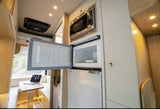RV rental interior featuring a compact kitchen with an open fridge/freezer, microwave, and a bright dinette.