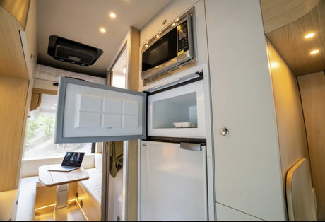 RV rental interior featuring a compact kitchen with an open fridge/freezer, microwave, and a bright dinette.