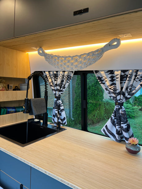 Cozy RV rental kitchen featuring a modern black sink, bamboo counter, and patterned curtains. Bright lighting & storage for an inviting space.