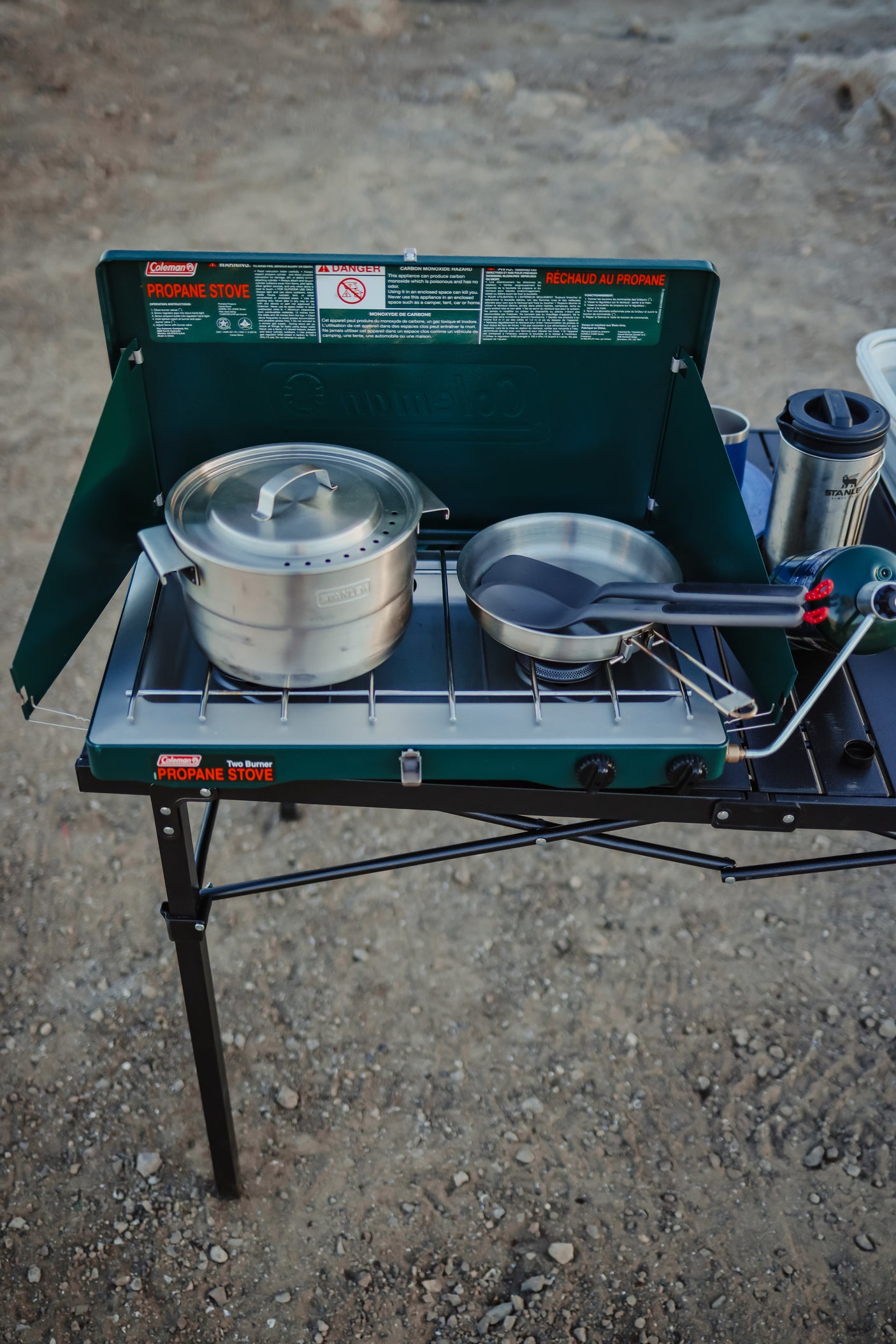 A Coleman two-burner propane stove with cookware on a portable stand, ready for outdoor cooking during an RV rental trip.
