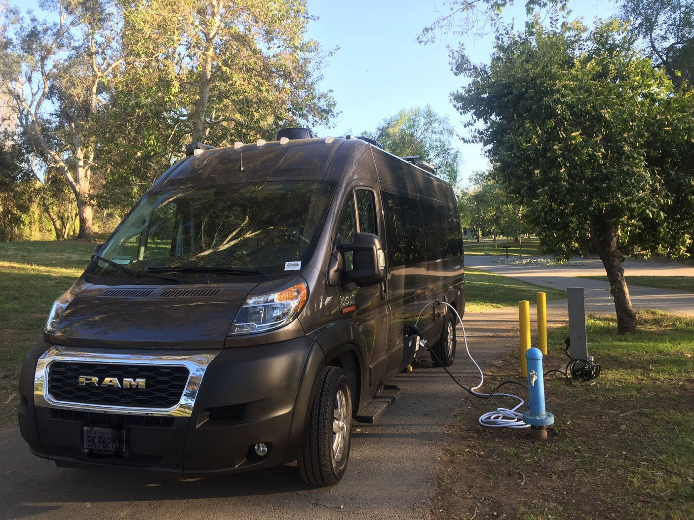 A dark Ram rv rental van is parked at a scenic campground, hooked up to water and power. Ideal for outdoor adventures.