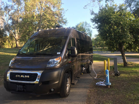 A dark Ram rv rental van is parked at a scenic campground, hooked up to water and power. Ideal for outdoor adventures.